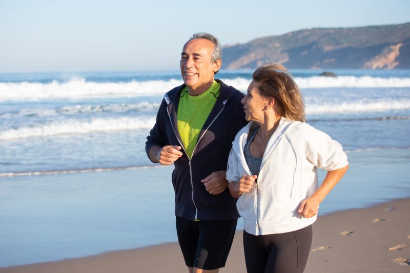 elderly couple jogging along the beach